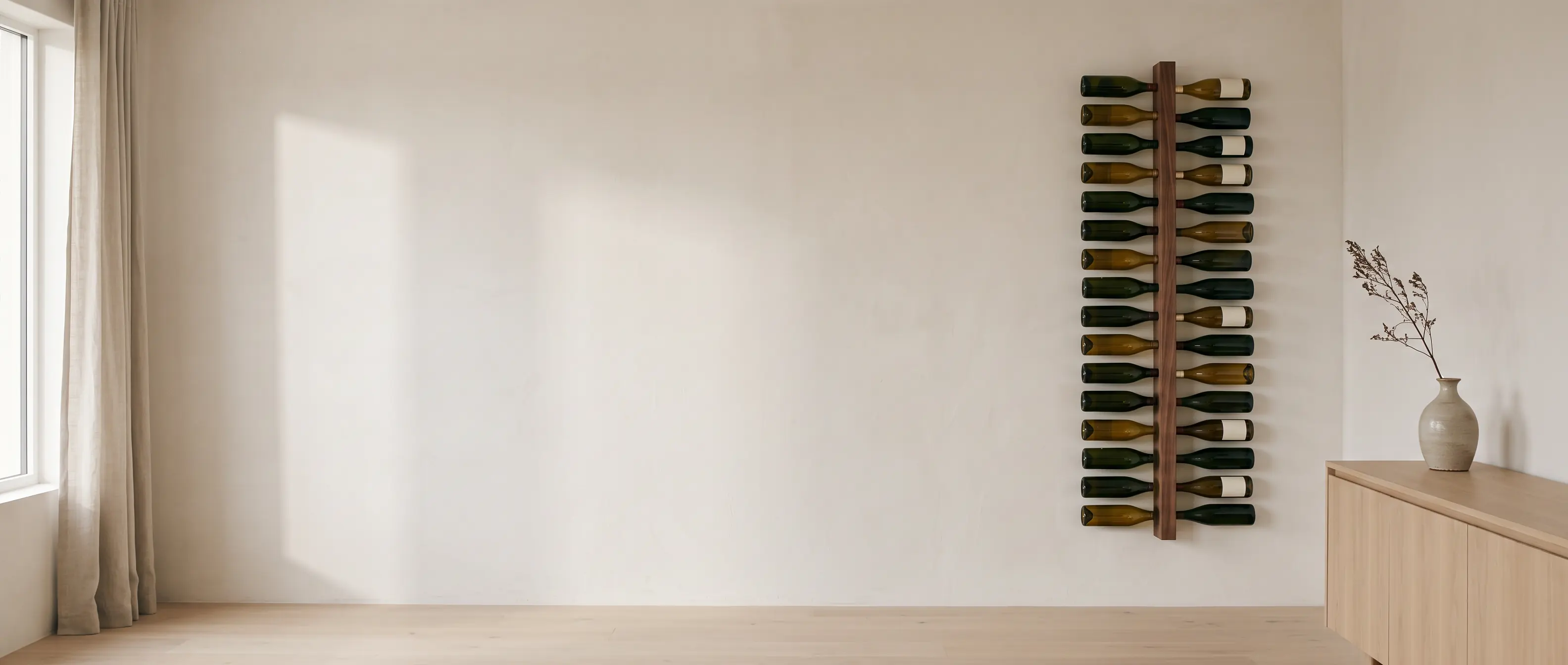 A tall walnut wall rack holding thirty-two wine bottles on their sides, on a warm white plaster wall in soft morning light, a pale oak sideboard beneath