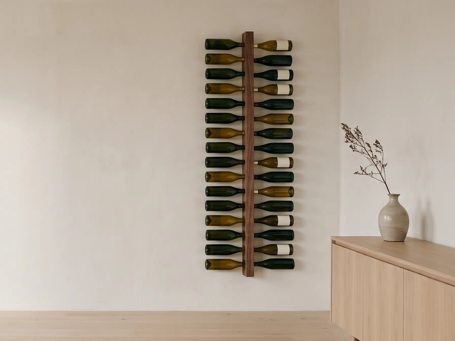 A tall walnut wall rack holding thirty-two wine bottles on their sides, on a warm white plaster wall beside a pale oak sideboard